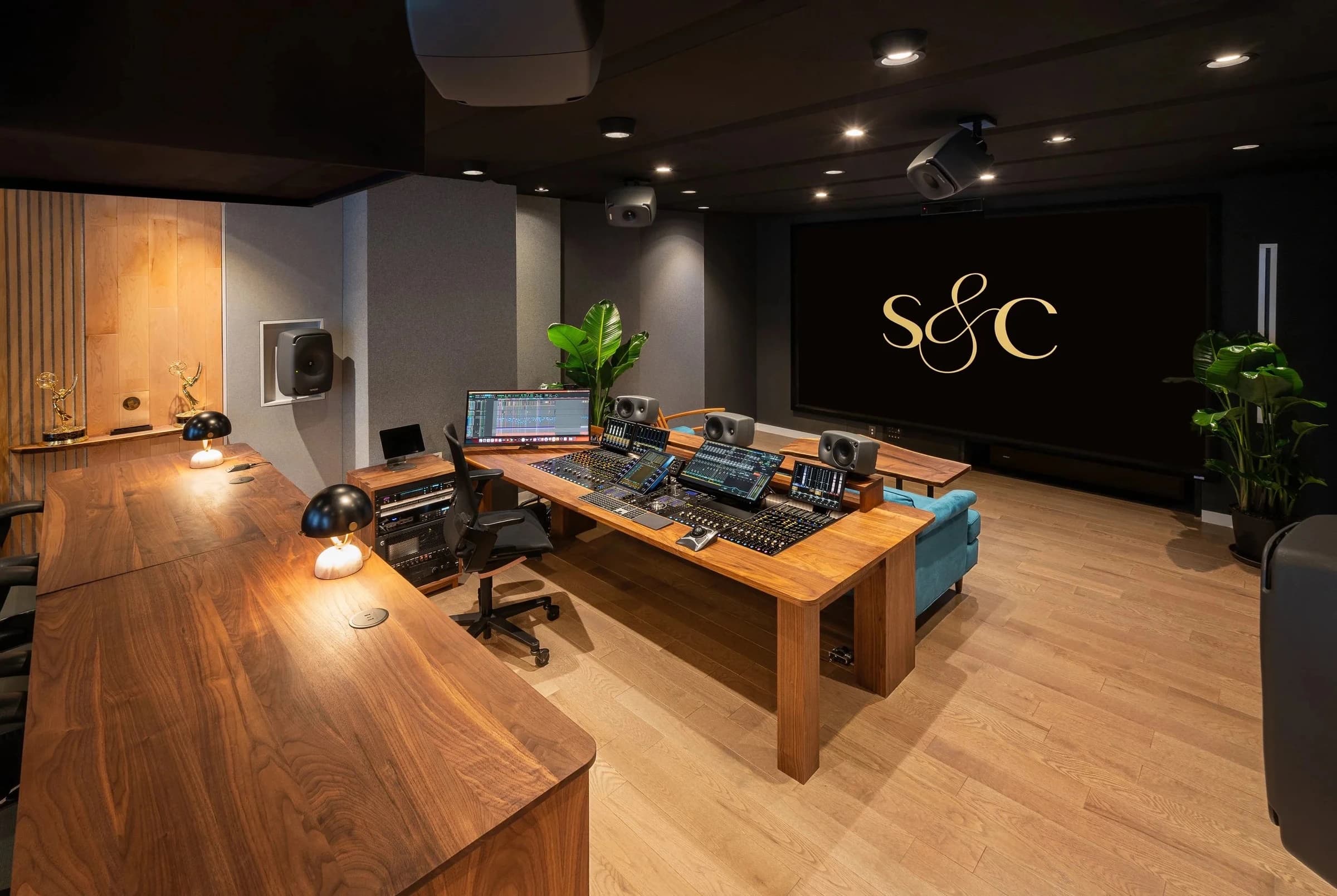 Studio A’s mix position, projection screen and producer seating, with overhead monitoring and wood finishes.