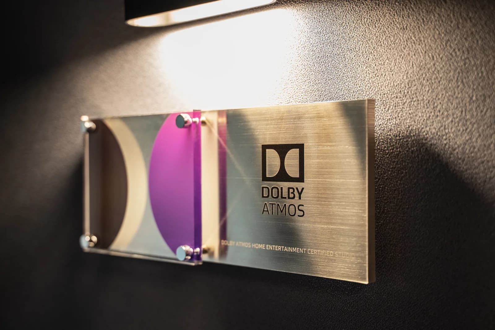 The Dolby Atmos Home Entertainment certification plaque beside a sconce in the sound lock.
